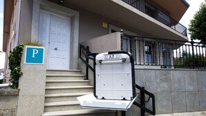 Een gebouw met een witte deur, een parkeerbord en een hellingbaan voor rolstoelen.