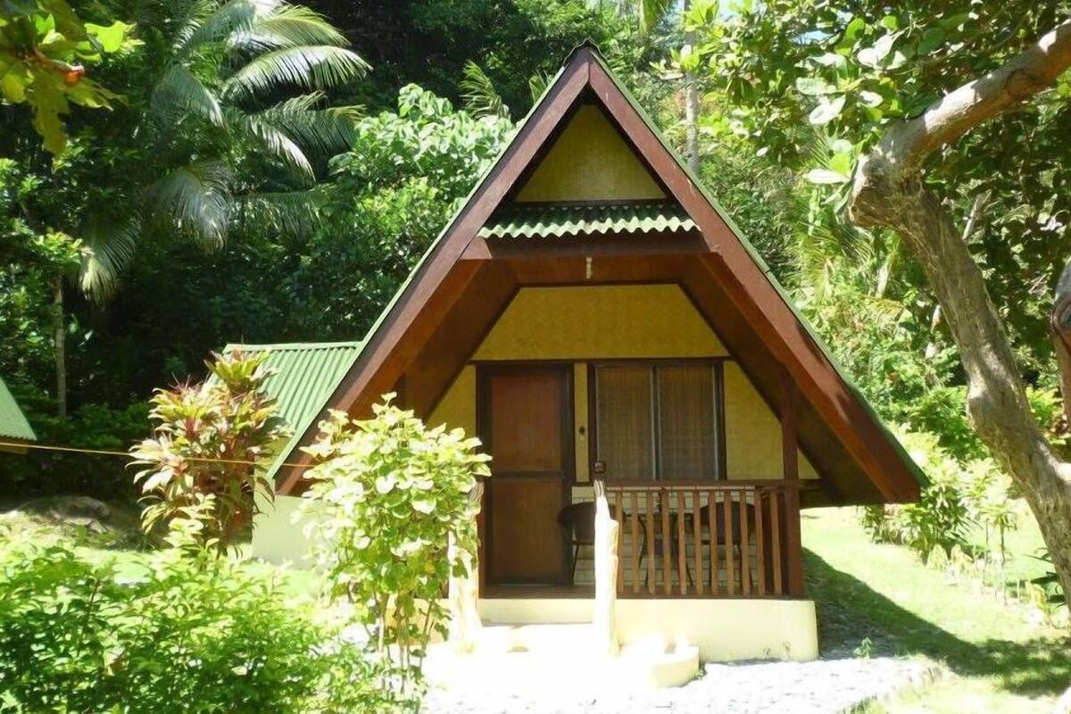 A small, single-story building with a triangular roof, surrounded by lush greenery.