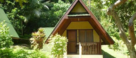 A small, single-story building with a triangular roof, surrounded by lush greenery.