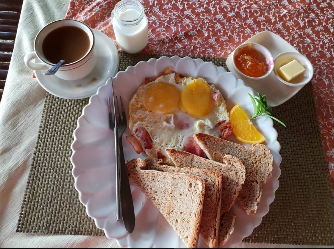 En morgenmadstallerken med æg, ristet brød, appelsinskiver og en kop kaffe på et bord med et mønstret dug.
