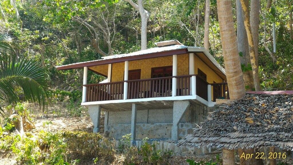 A two-story building with a balcony, surrounded by trees and vegetation.