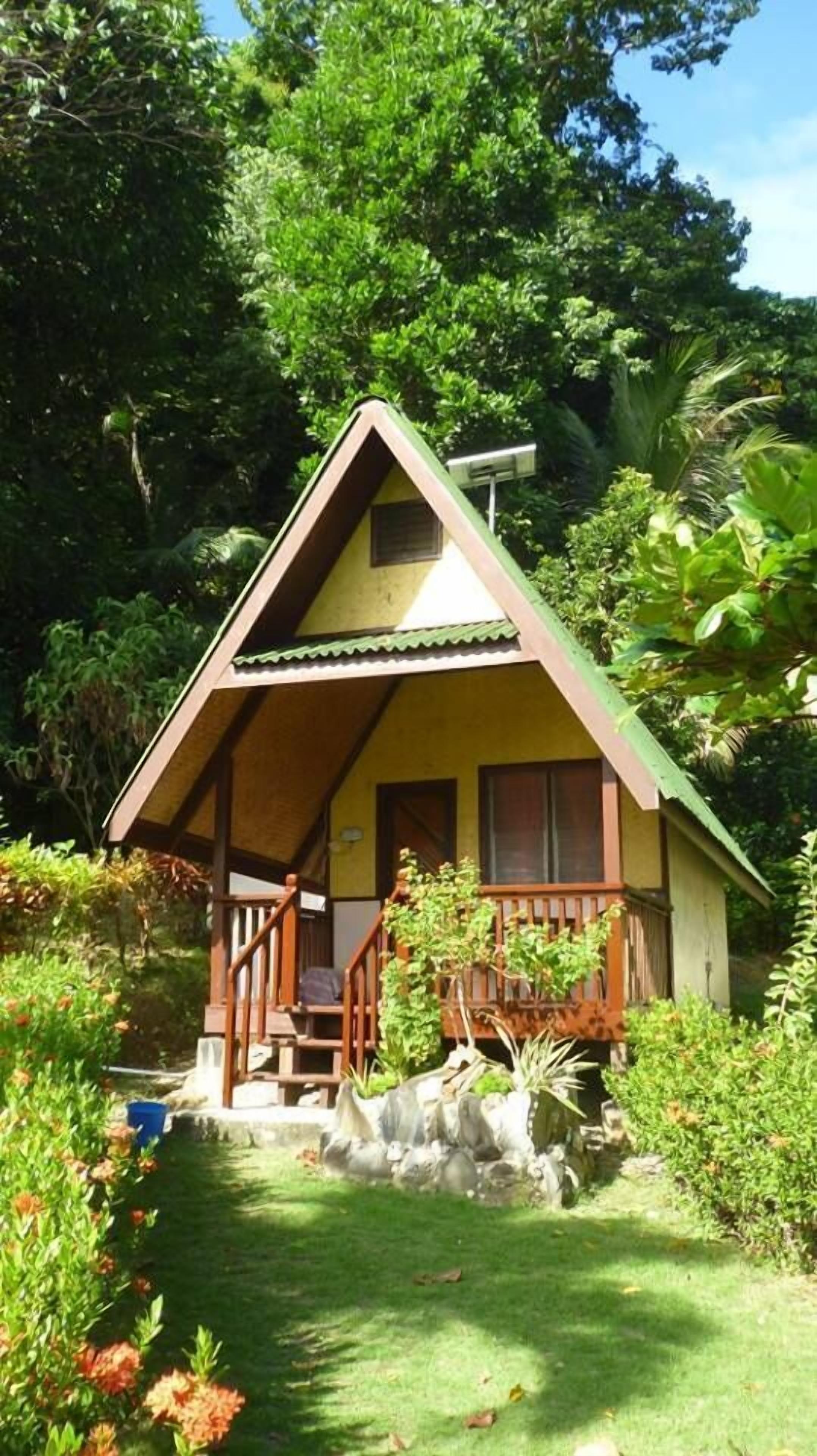 Una casa pequeña de un solo piso con techo inclinado, un porche con escaleras y una ventana pequeña.