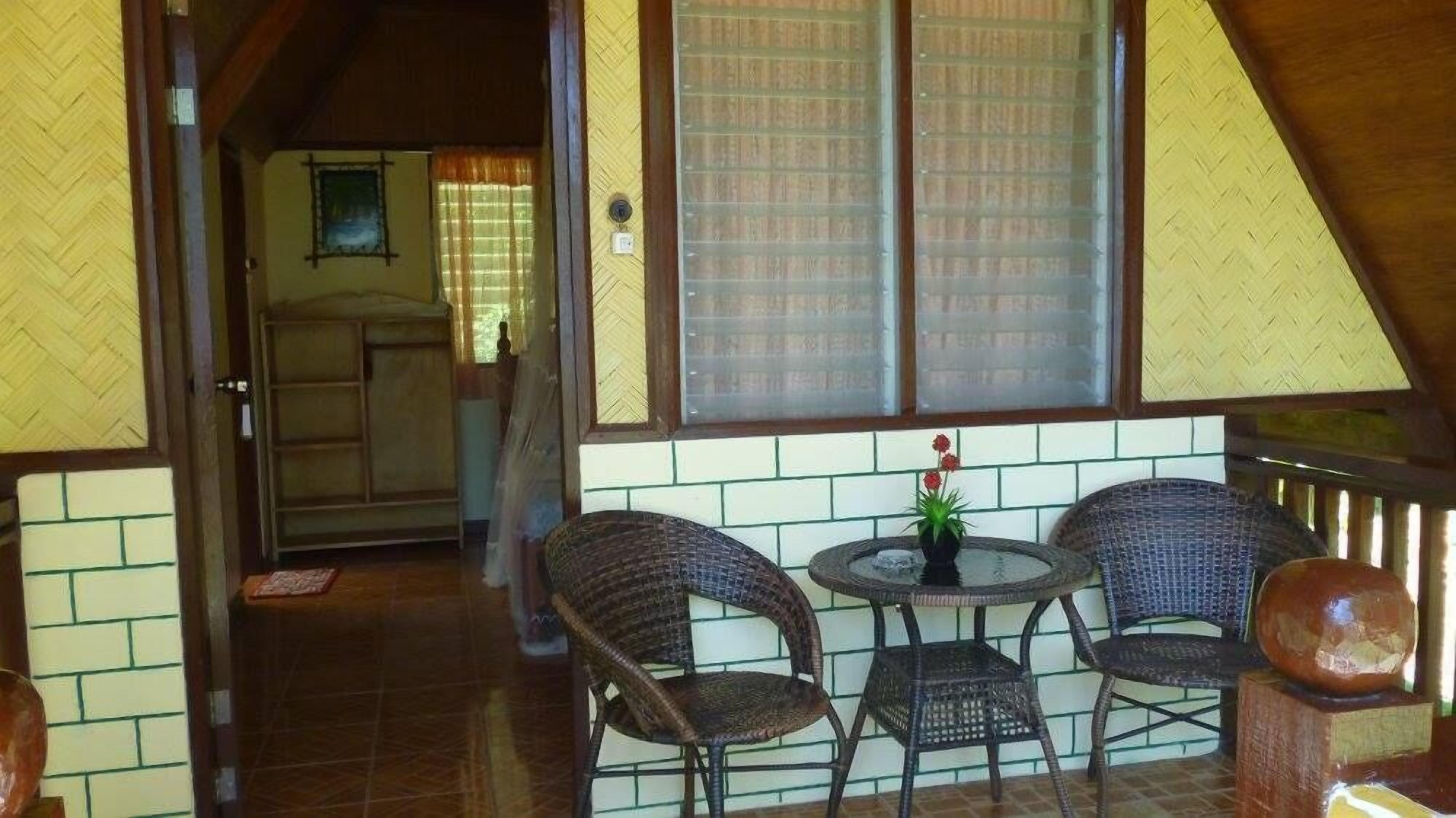 A cozy room with wicker chairs and a small table, a window with blinds, and a door leading to another room.