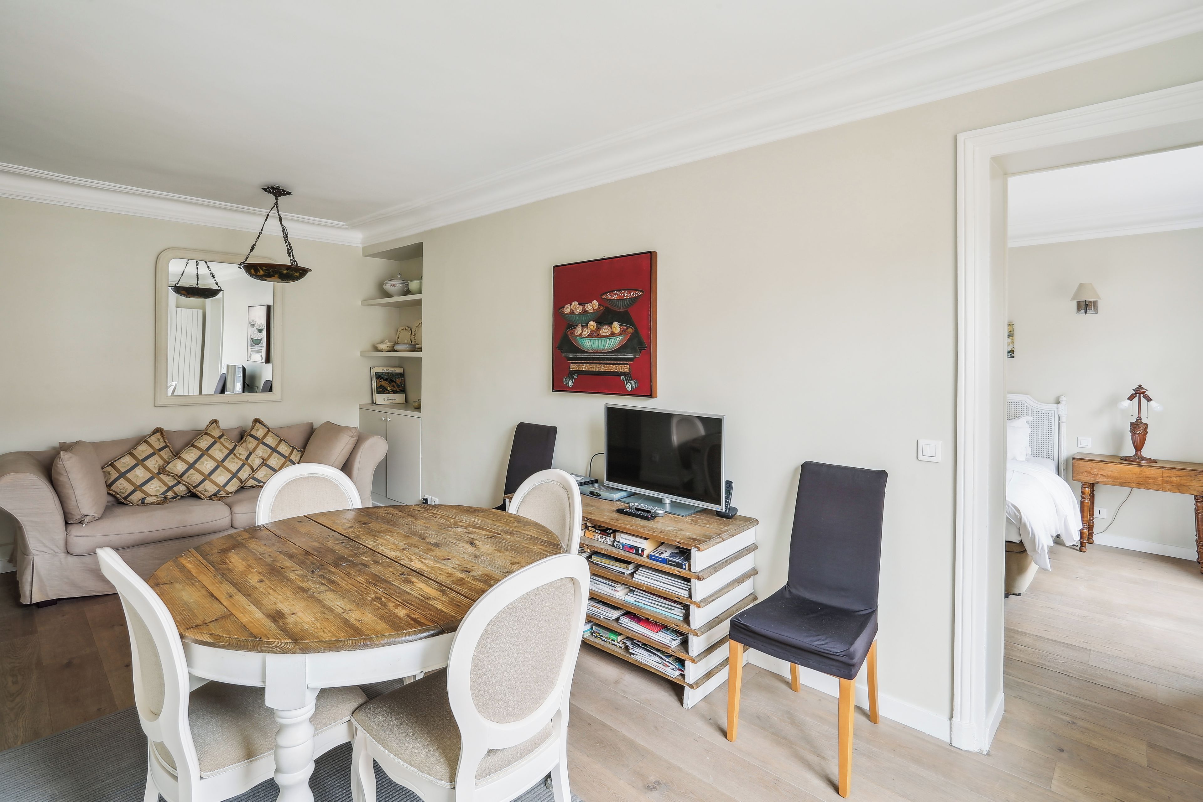 A living room with a round wooden table, white chairs, a sofa, a television, and a bookshelf.