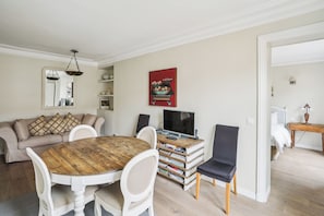 A living room with a round wooden table, white chairs, a sofa, a television, and a bookshelf. - ID 233 - Marais / rue Portefoin (Paris)