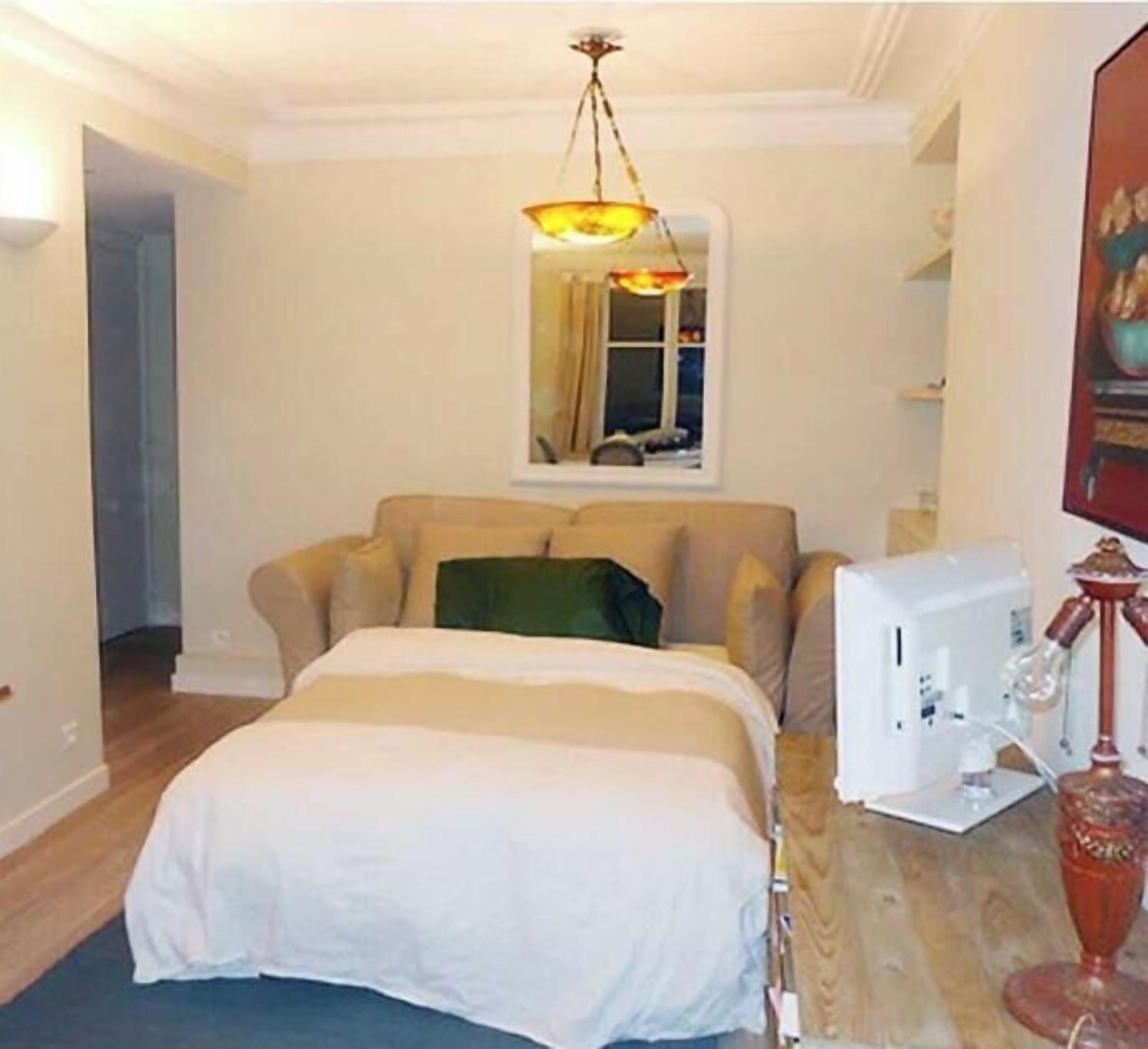 A bedroom with a bed, a desk with a sewing machine, a lamp, and a painting on the wall.