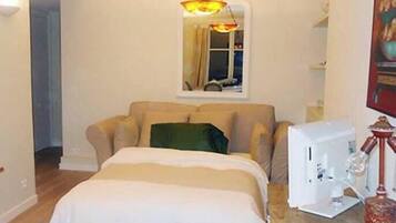 A bedroom with a bed, a desk with a sewing machine, a lamp, and a painting on the wall.