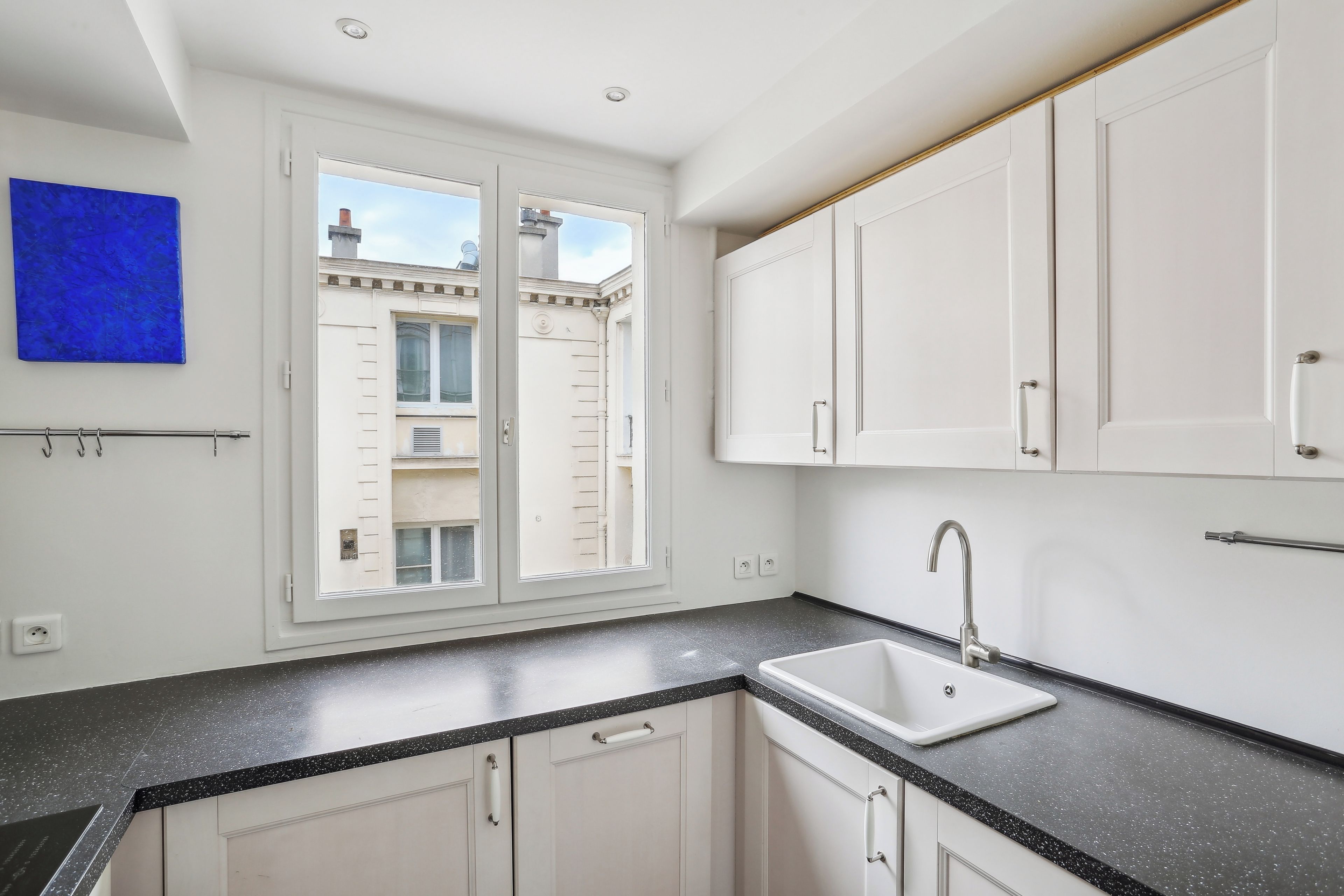 A modern kitchen with white cabinets, a black speckled countertop, a built-in sink, and a window with a view of buildings outside.
