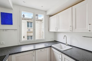A modern kitchen with white cabinets, a black speckled countertop, a built-in sink, and a window with a view of buildings outside. - ID 233 - Marais / rue Portefoin (Paris)