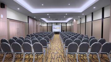 A conference room with rows of chairs, a projection screen, and a carpeted floor.