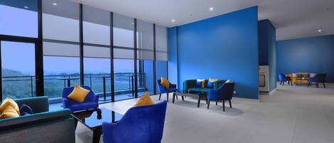 Un moderno vestíbulo de hotel con paredes azules, ventanas amplias y un balcón con vistas.