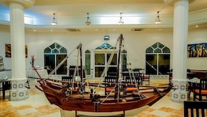A spacious hall with a large wooden boat model, white columns, and arched windows. - Samharam Resort Salalah (Salalah)