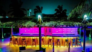 A tropical bar area with wooden stools and a bar counter, surrounded by palm trees and a thatched roof structure. - Samharam Resort Salalah (Salalah)