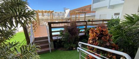 A rooftop terrace with a wooden pergola, artificial grass, and various potted plants.