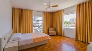 A bedroom with a bed, a chair, a ceiling fan, and a window with curtains. - Hotel Centenário (Tramandai)