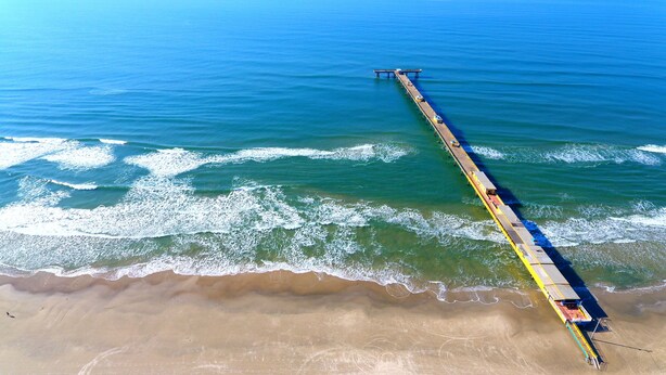 An aerial view of a long pier extending into the ocean, with waves crashing onto the shore. - Hotel Centenário (Tramandai)