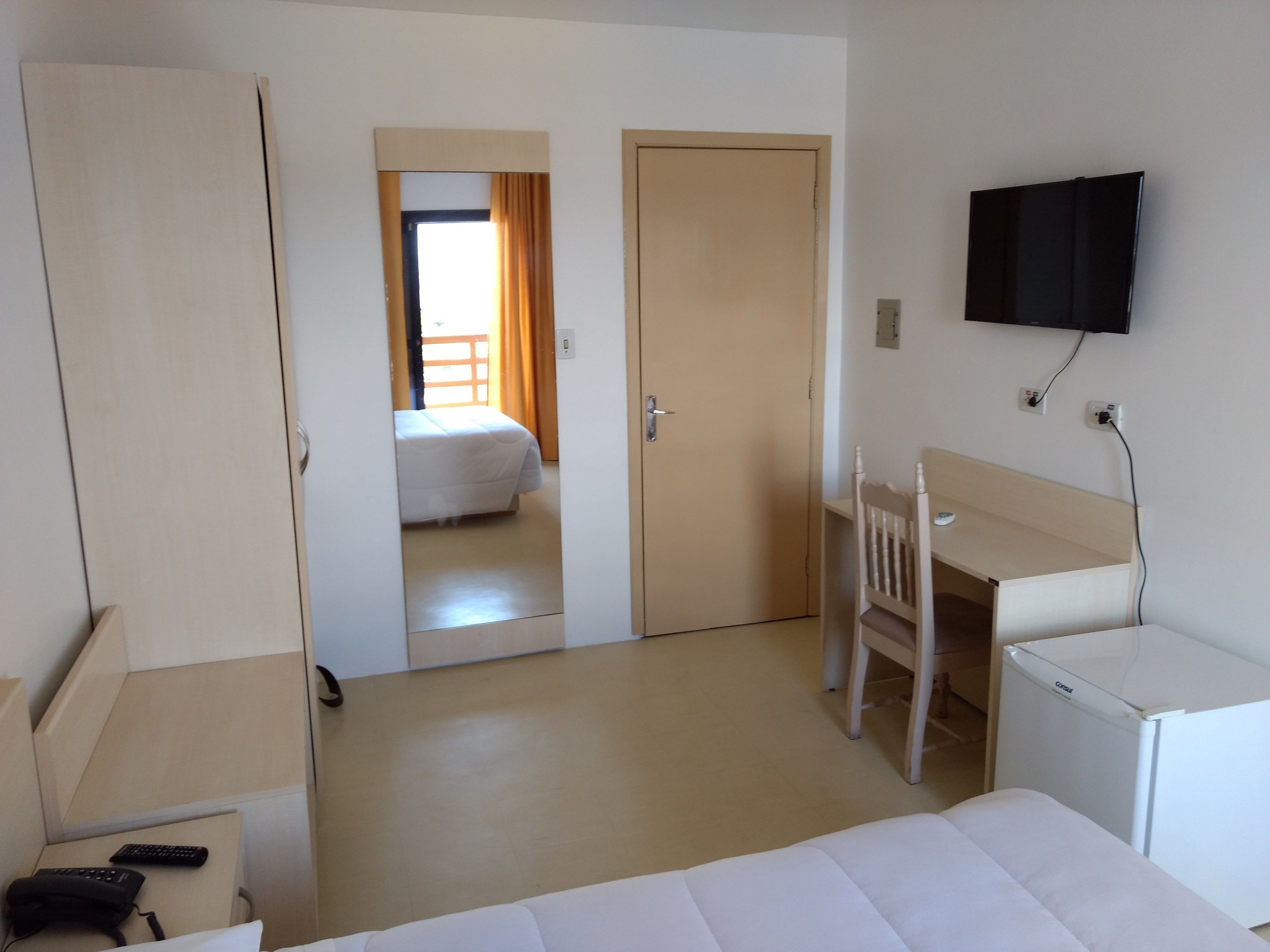 Una habitación de hotel con cama, escritorio, silla, televisión y armario.