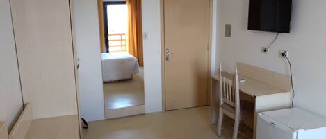 A hotel room with a bed, a desk, a chair, a television, and a wardrobe.