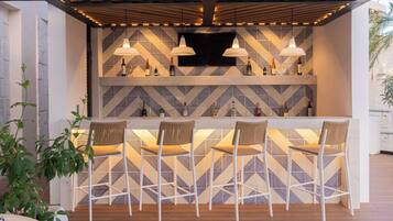 A bar area with a geometric patterned wall, white bar stools, and pendant lighting.