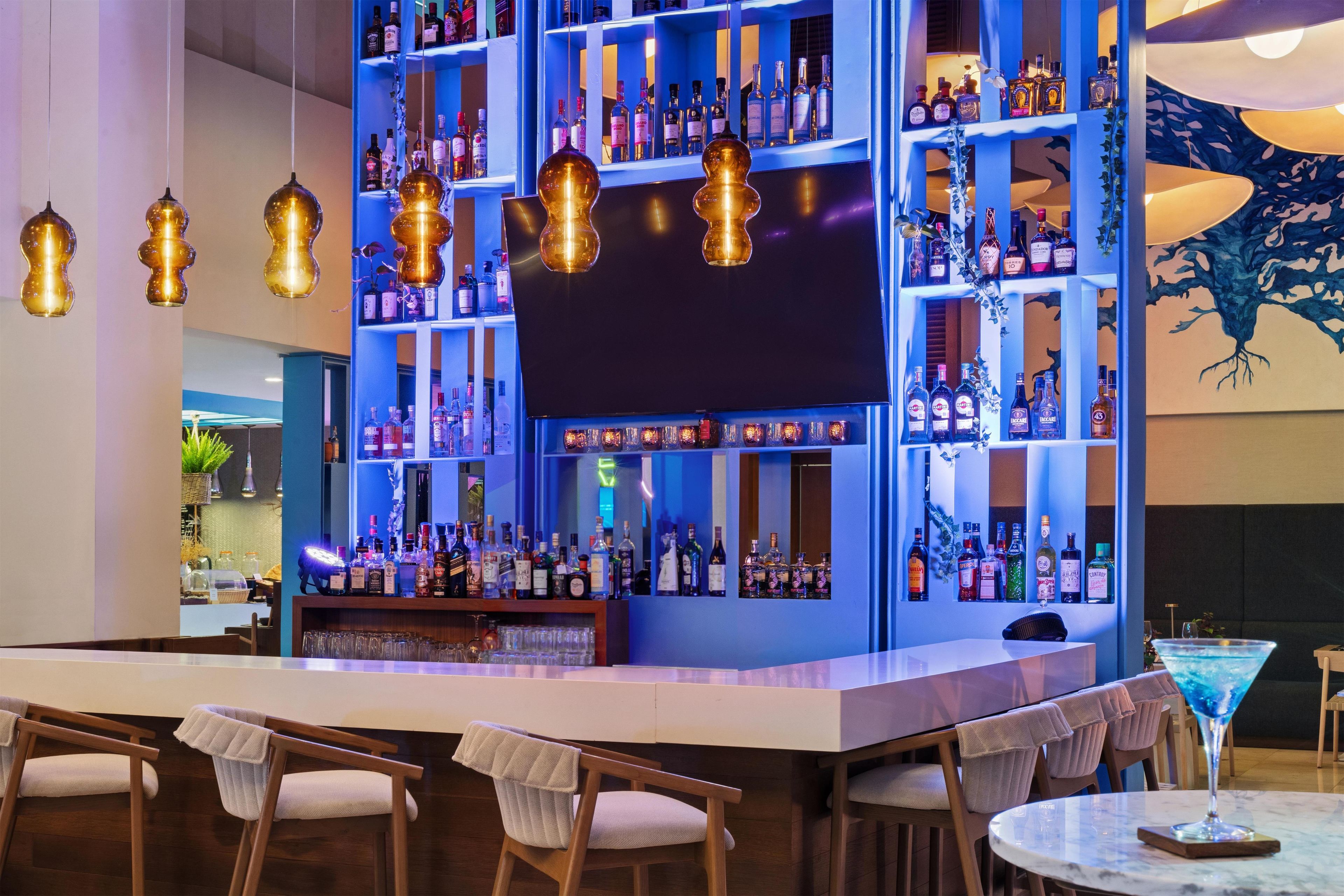 A bar area with multiple shelves of liquor bottles, hanging pendant lights, and bar stools.