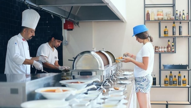 A buffet setup with multiple food stations and a person serving food. - Simply Fine Hotel Alize - Adults Only (Alanya)