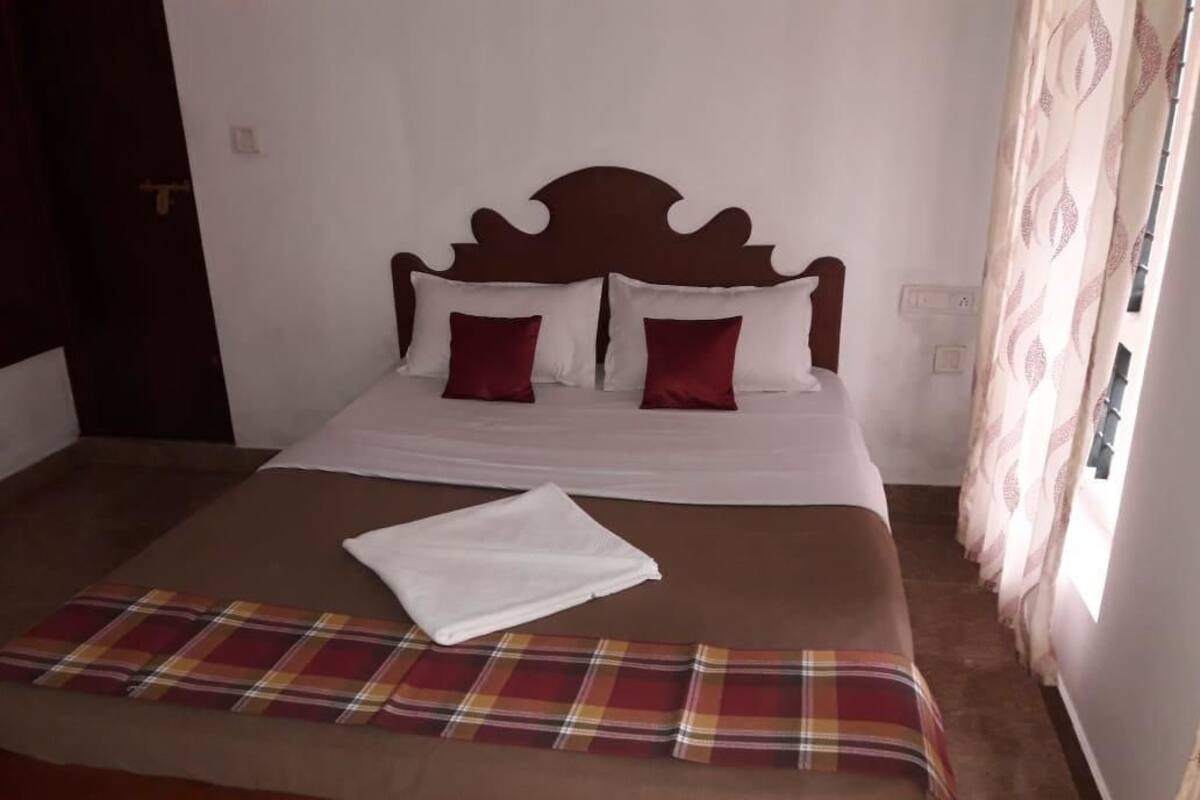 Una cama bien tendida con una manta escocesa y dos almohadas, un cabecero de madera y una ventana con cortinas.