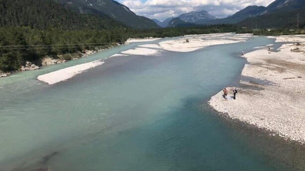 Um rio com uma praia arenosa e montanhas ao fundo.