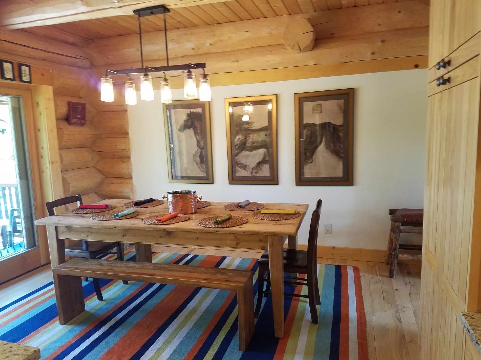 A wooden dining table with a bench, surrounded by chairs, in a room with wooden walls and ceiling.
