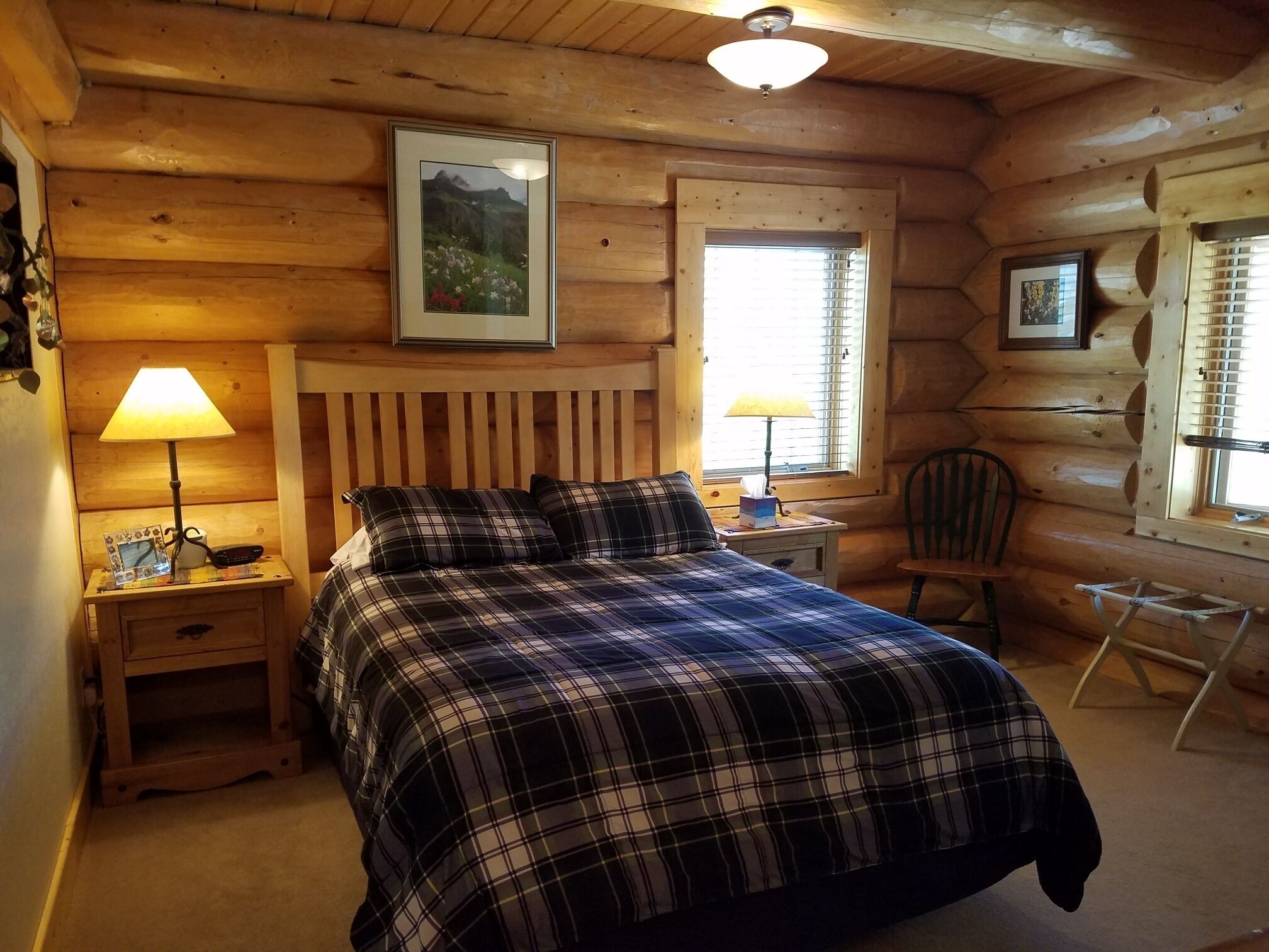 Um quarto de cabana de tronco acolhedor, com uma cama, duas luminárias de cabeceira, uma cadeira e quadros nas paredes.