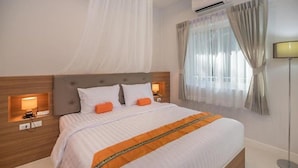 Ein Hotelzimmer mit einem großen Bett, einem Nachttisch mit Lampe, einer Wandklimaanlage und einem Fenster mit Vorhängen.