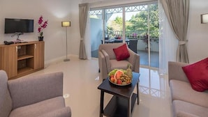 Ein modernes Wohnzimmer mit einer Couch, einem Couchtisch mit Obst, einem Fernseher und einem Balkon mit Vorhängen.