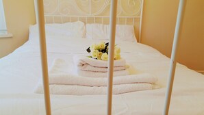 A bed with white linens, a metal headboard, and a bouquet of yellow flowers on a folded towel. - The Hazeldene Apartment (Cardiff)