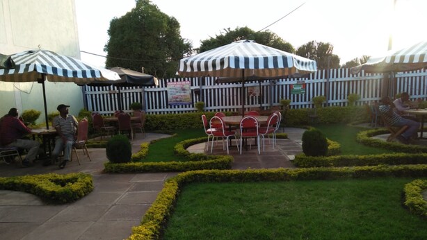 An outdoor patio area with tables and chairs, surrounded by neatly trimmed hedges and a white picket fence. - Mt Kenya Safari Halt Hotel (Chaka)
