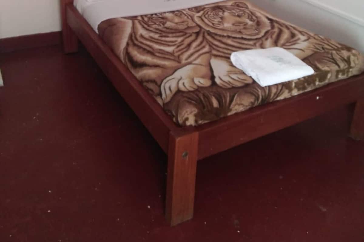 Un lit simple avec une couvre-lit à motifs floraux, une tête de lit en bois et un baldaquin blanc.