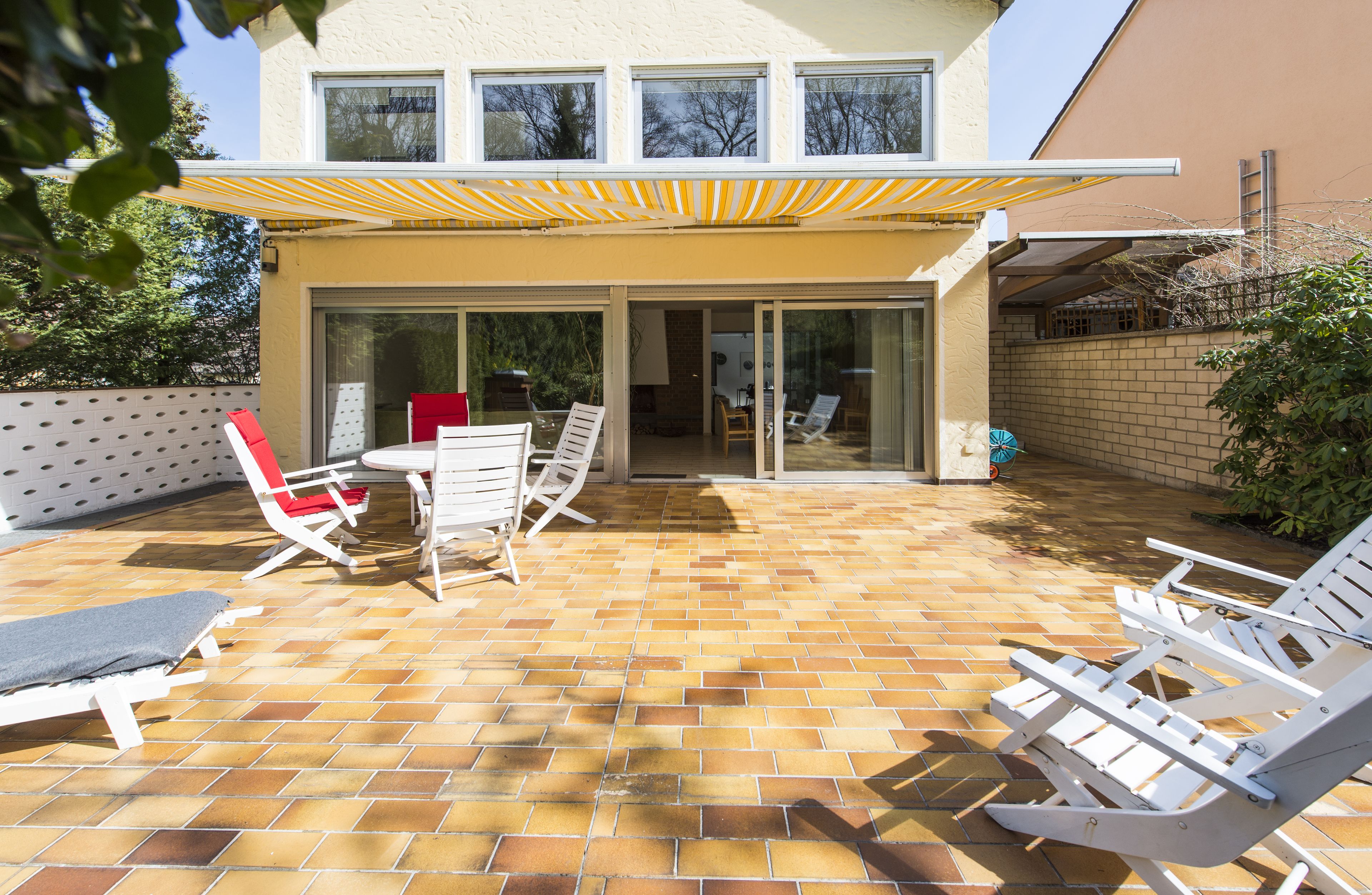 A patio area with a brick floor, white lounge chairs, a table with chairs, and a yellow awning.