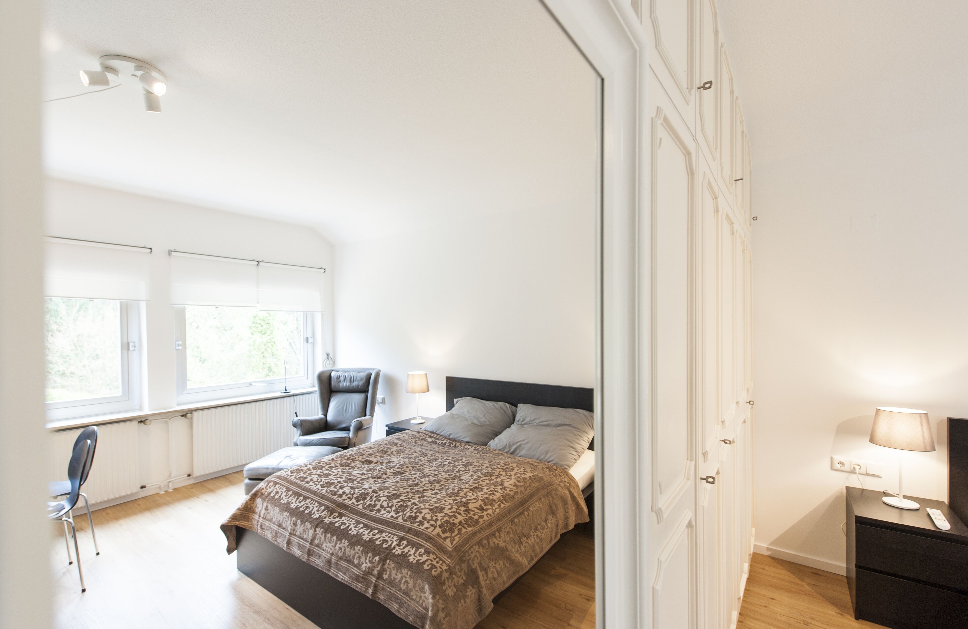 A bedroom with a bed, a chair, a nightstand, and a window.