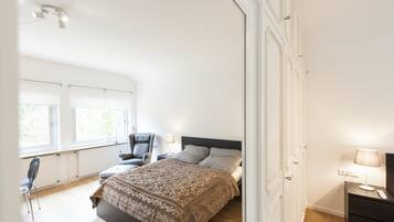 A bedroom with a bed, a chair, a nightstand, and a window.