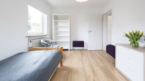 Quarto moderno com cama, guarda-roupa branco, um banquinho roxo e janela com persianas.