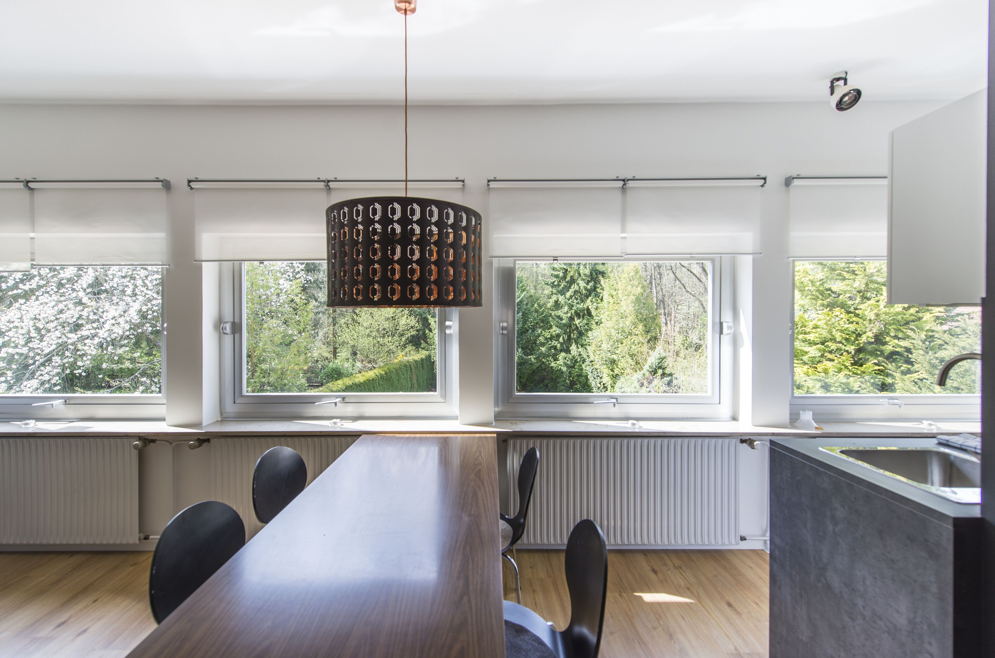 Una cocina moderna con una mesa de comedor grande, varios ventanales y una lámpara colgante.