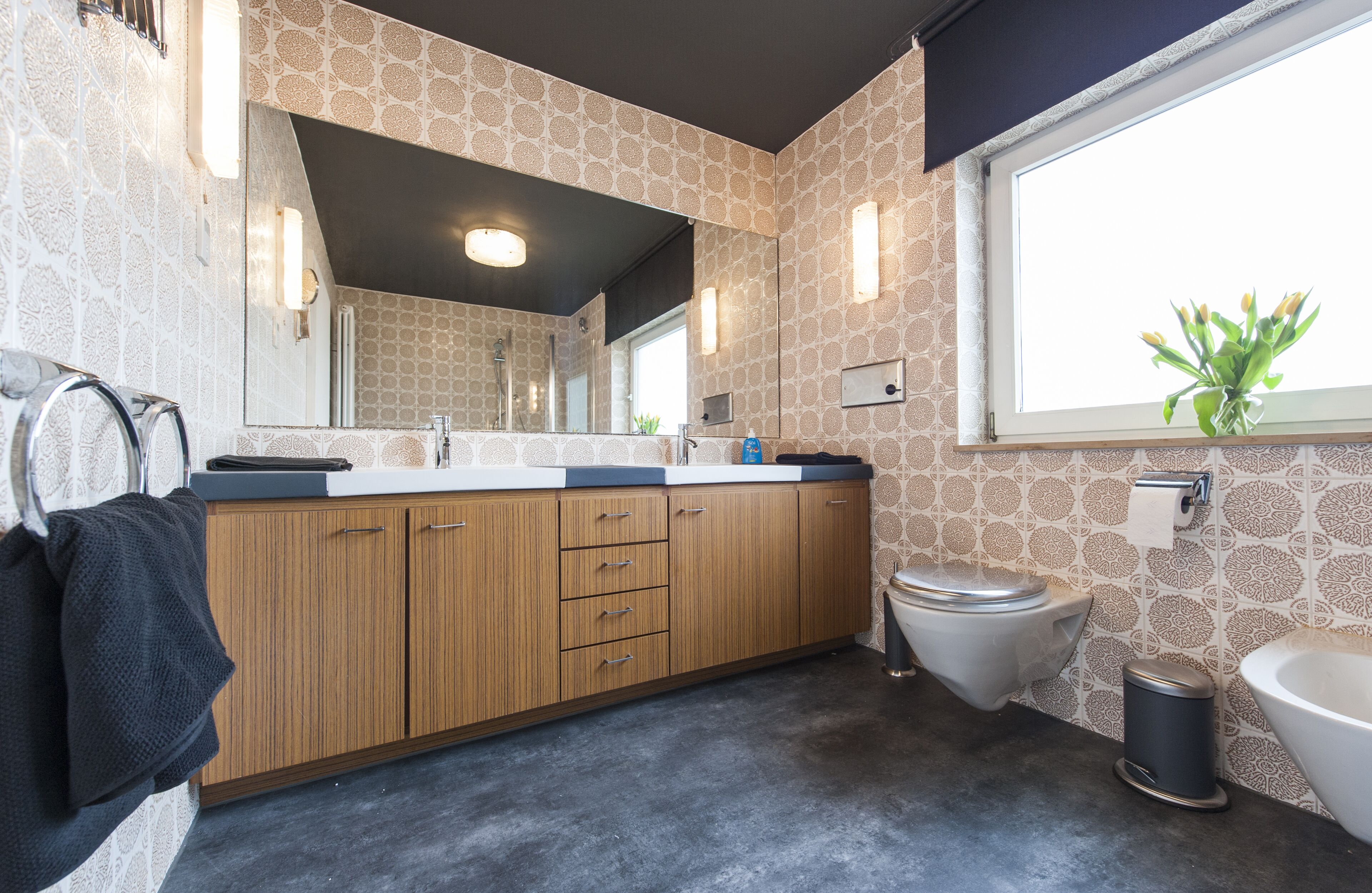 A modern bathroom with a large mirror, wooden cabinets, a toilet, and a bathtub.