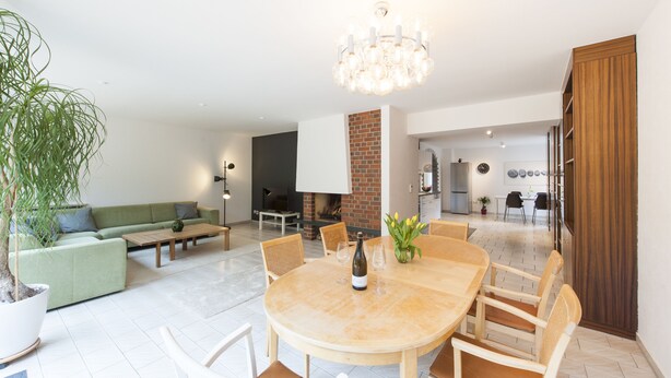 Uma sala de estar moderna com uma mesa de jantar redonda de madeira, um sofá verde e um vaso com planta.