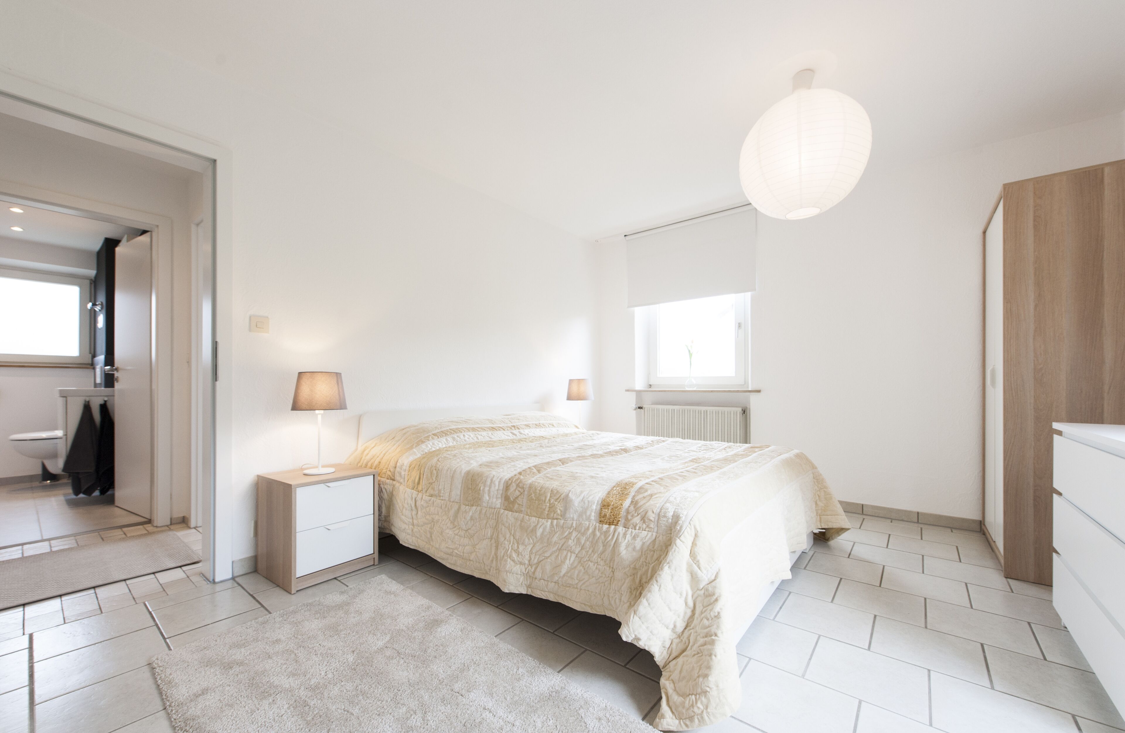 Um quarto com uma cama, mesas de cabeceira, um abajur, um radiador e um guarda-roupa.