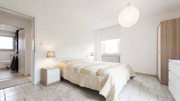 Um quarto com uma cama, mesas de cabeceira, um abajur, um radiador e um guarda-roupa.