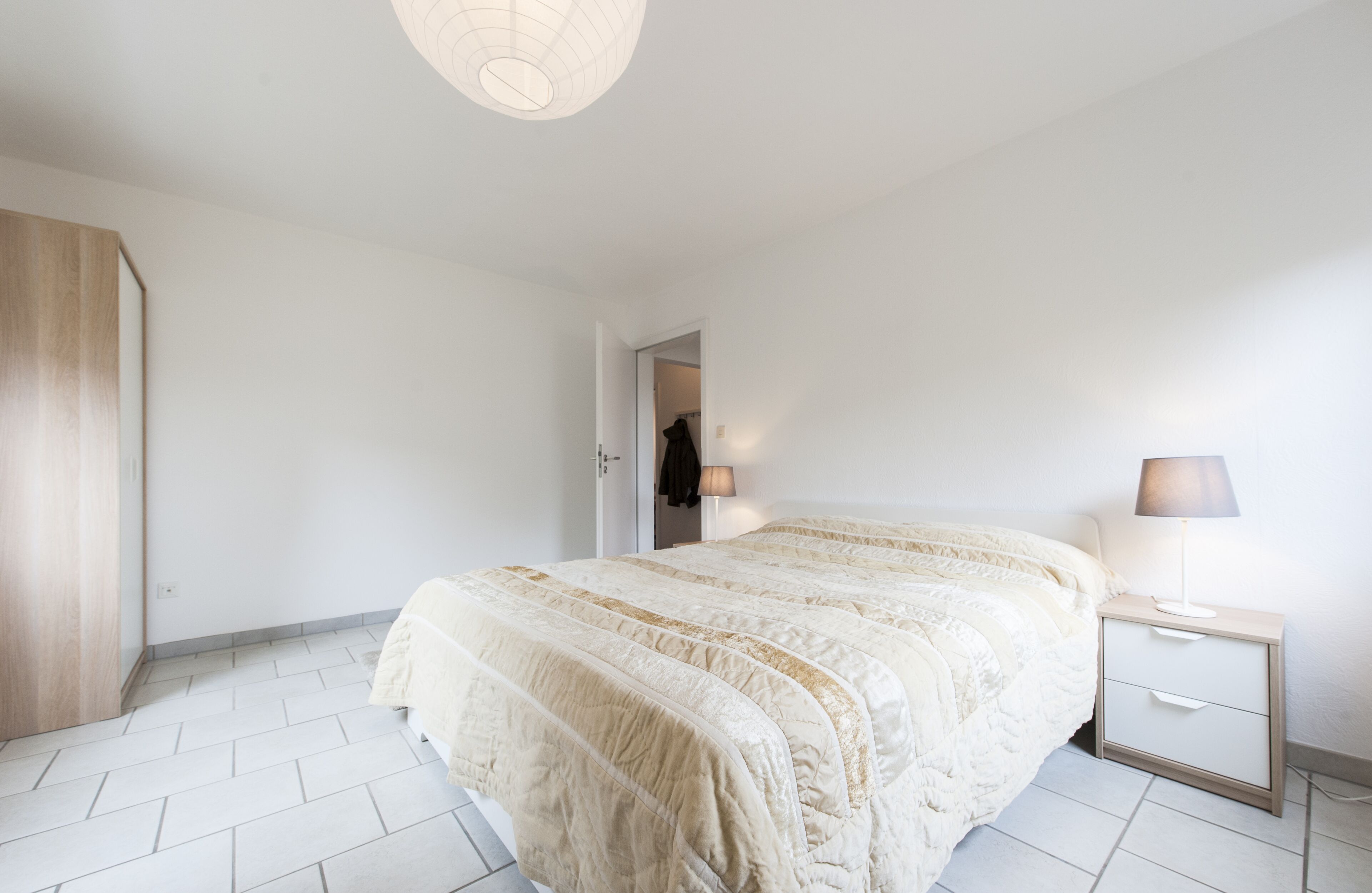 A bedroom with a large bed, a bedside table with a lamp, and a wardrobe.