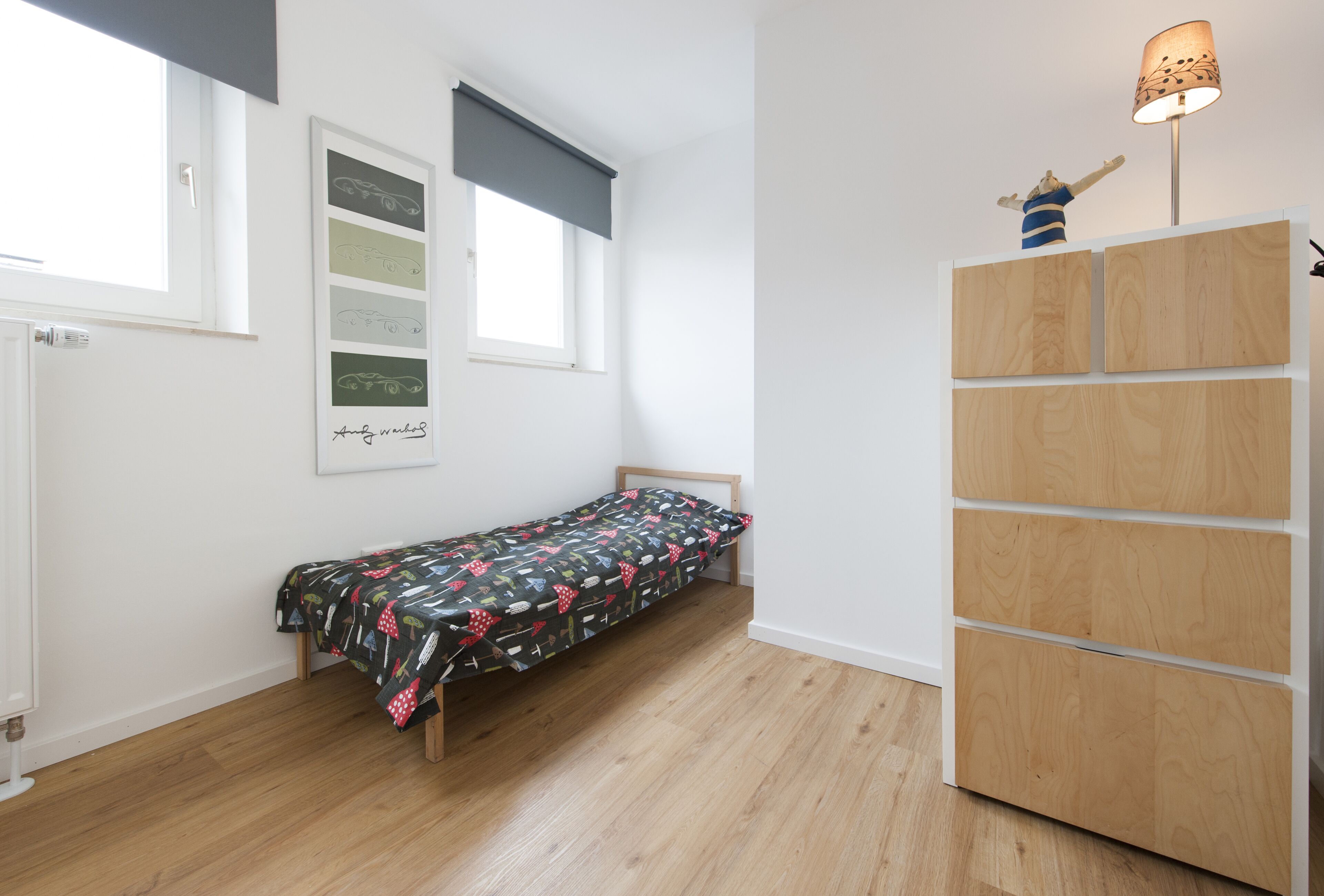 Una habitación pequeña con cama individual, piso de madera, mesita de noche, armario y ventana con persianas.