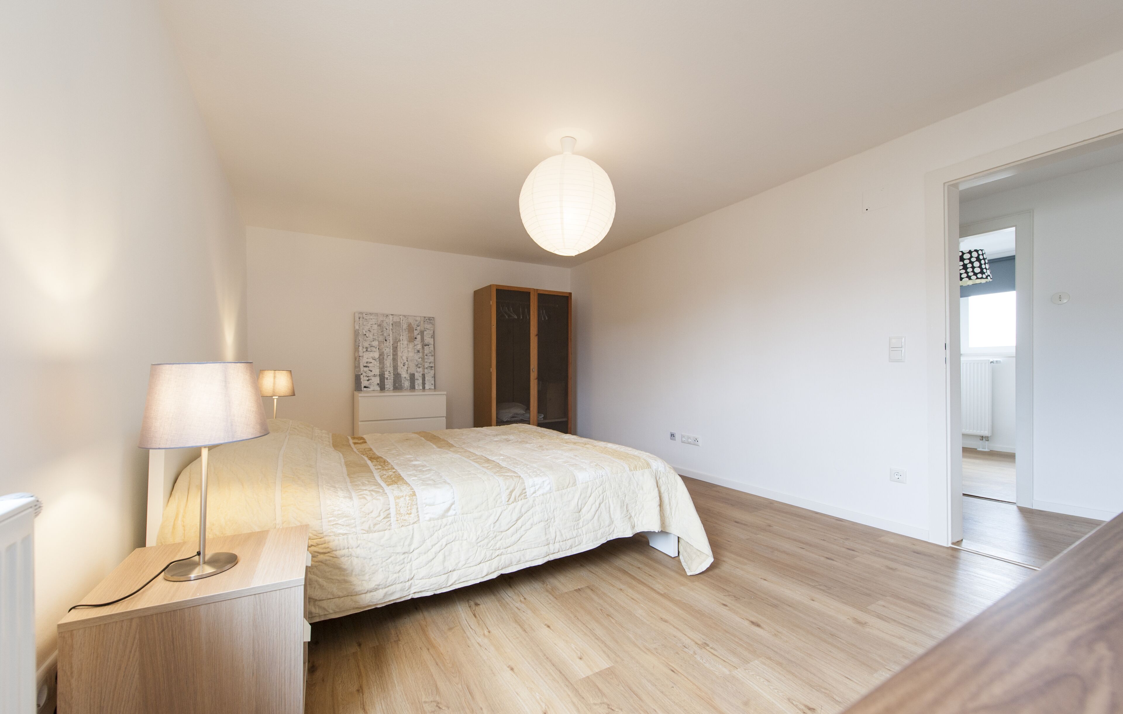 Ein Schlafzimmer mit einem Bett, Nachttischlampen, einem Nachtisch, einem Holzschrank und einer Pendelleuchte.