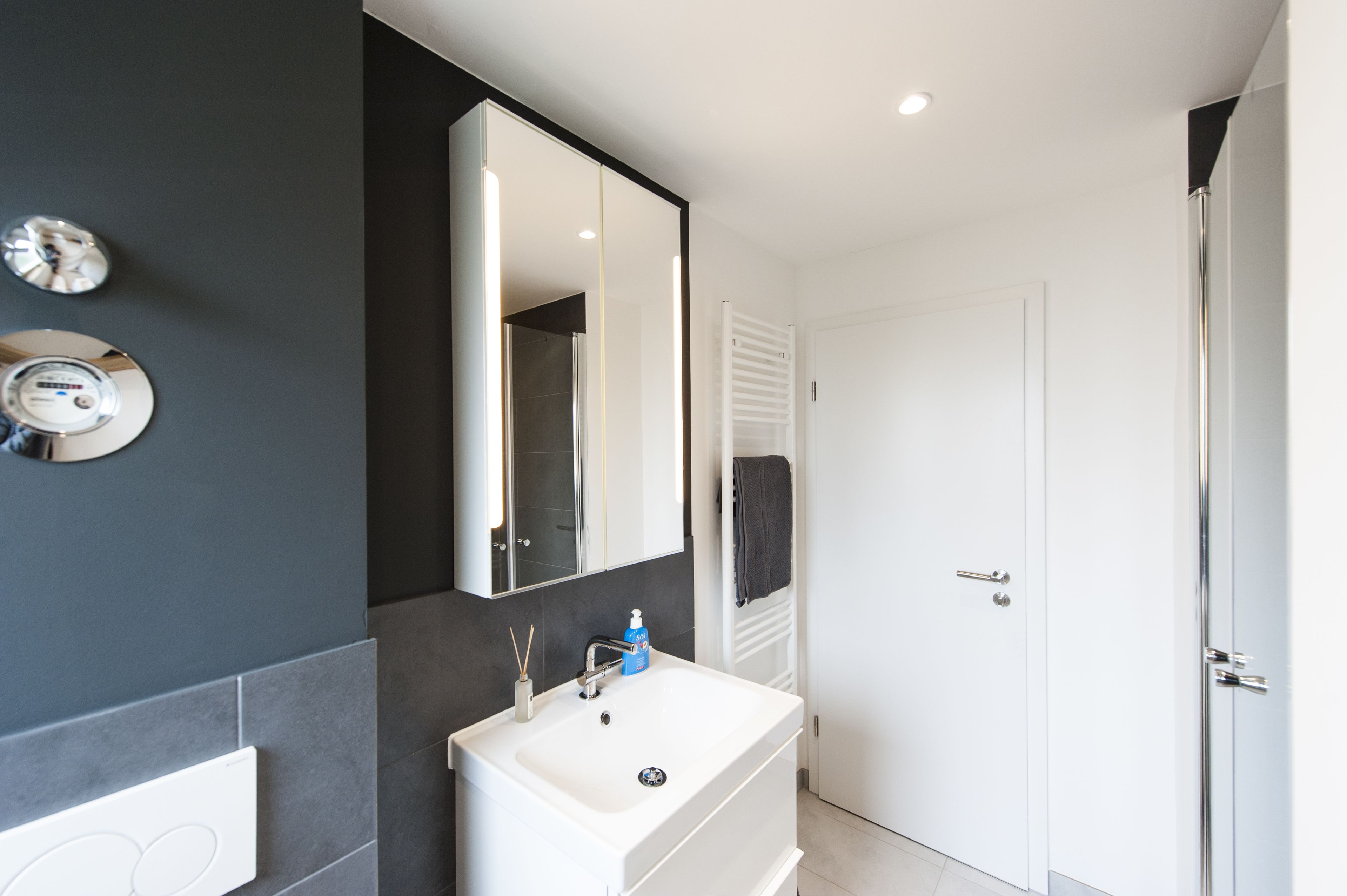 A modern bathroom with a white sink, a large mirror, and a towel rack.