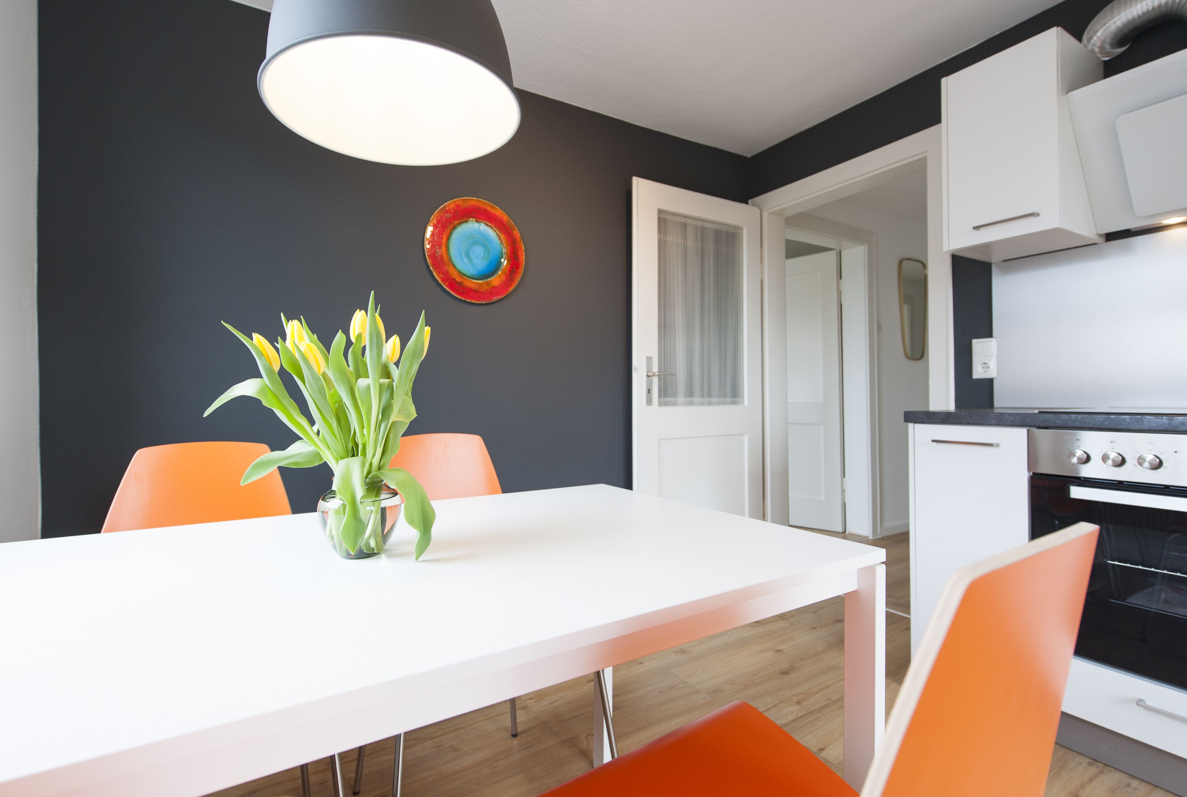 Une cuisine moderne avec des meubles blancs, un four noir et une table à manger blanche, agrémentée de chaises orange.