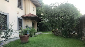 Uma casa com telhado de cerâmica, varanda pequena e gramado bem cuidado.