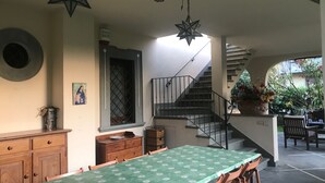 Uma área de refeições com uma mesa comprida, armários de madeira e uma escada que dá para um pátio externo.